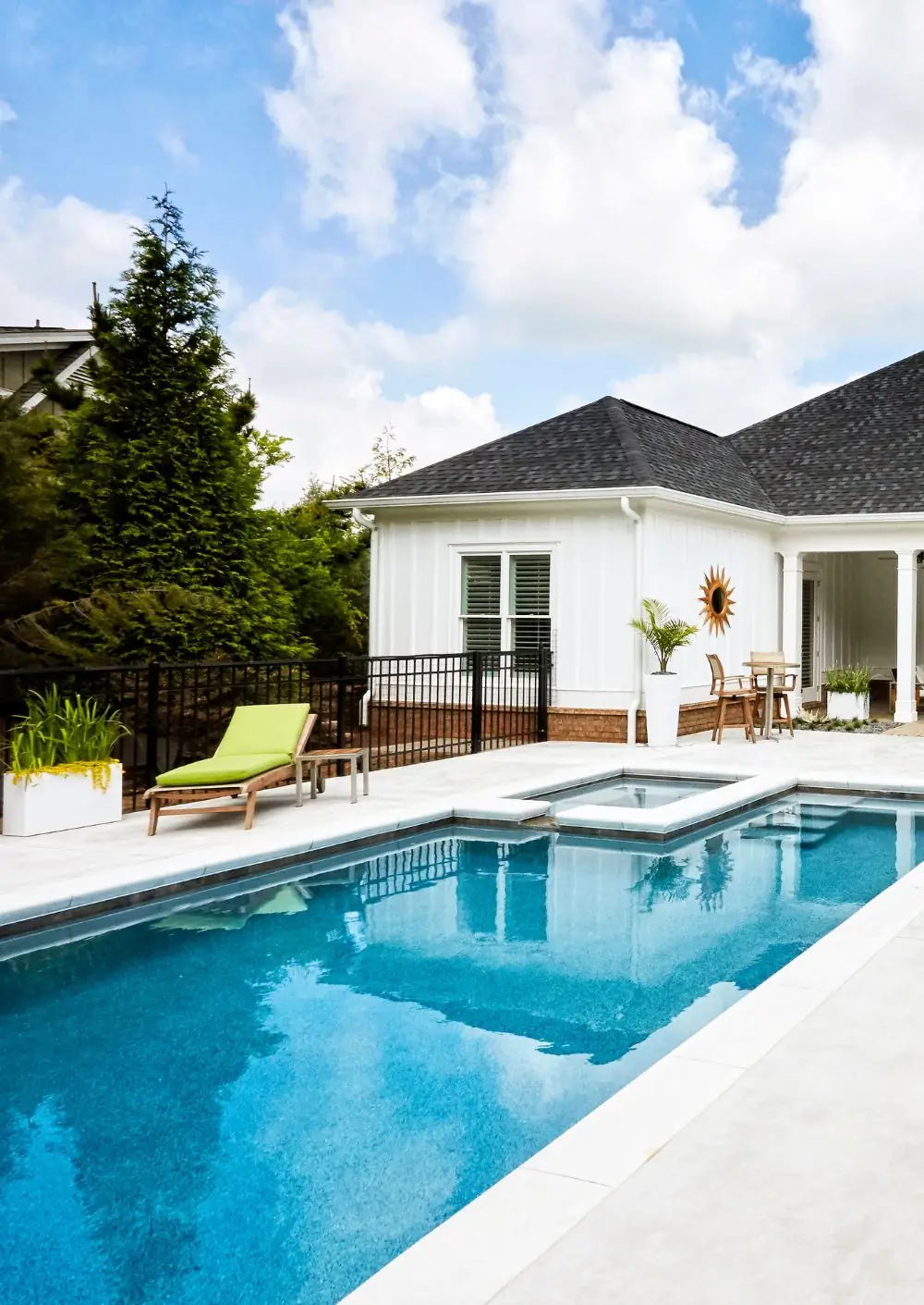 Rectangular pool with an attached spa behind a white farmhouse-style home