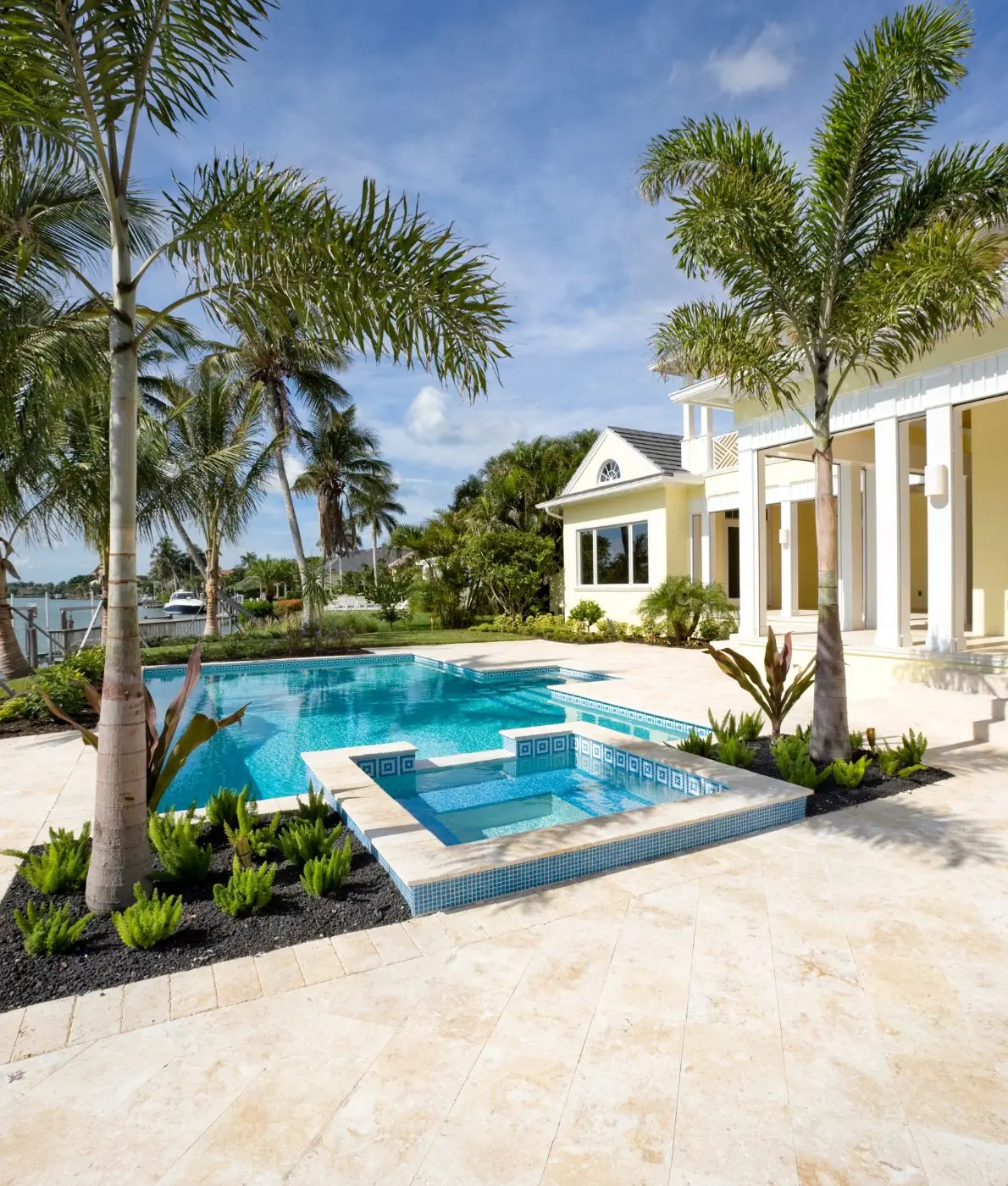 Pool with a raised mosaic-tile spa and travertine deck beside a waterfront home