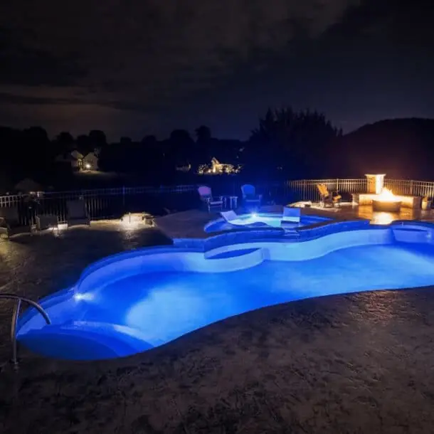 Freeform fiberglass pool lit blue at night