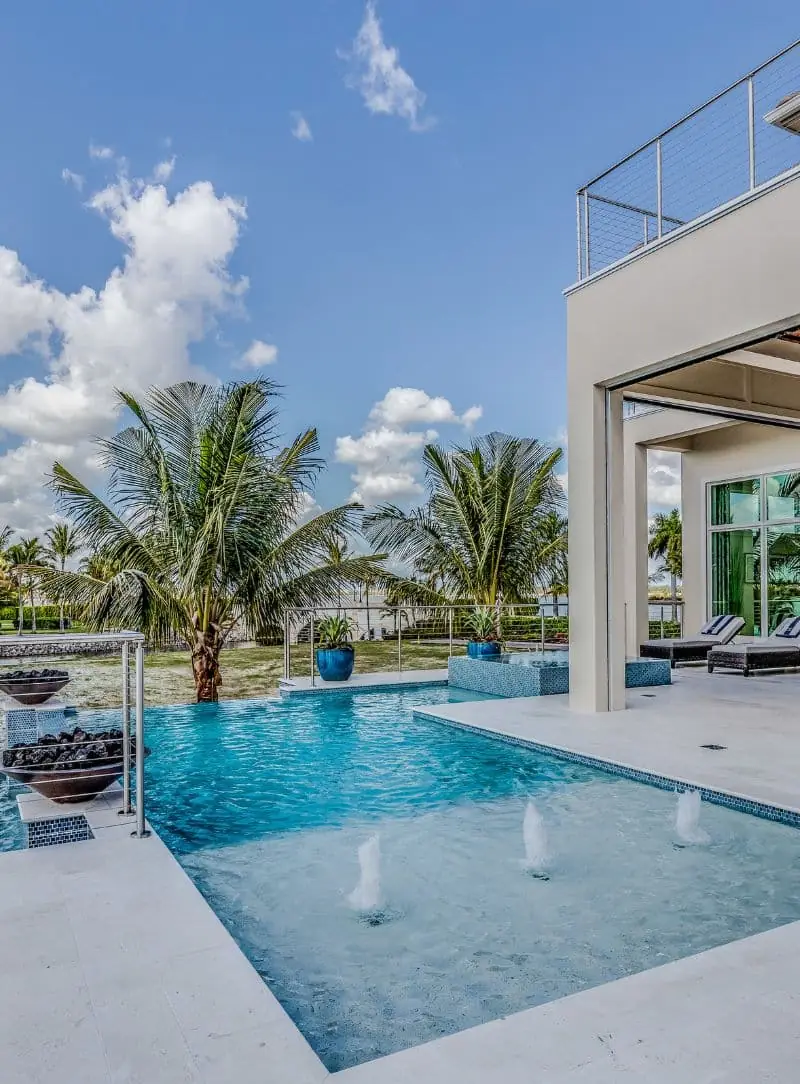 Modern pool with fountain jets beside a home with a rooftop deck