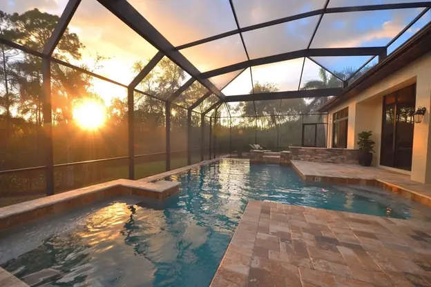 Screened pool with a sun shelf and travertine deck at sunset