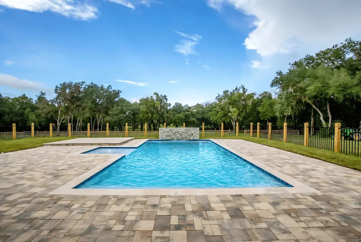Rectangular pool with an attached spa and stone water wall on a paver deck